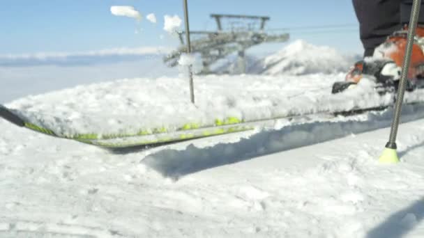 SLOW MOTION SULJE Up: Hiihtäjä puhdistaa tuoretta lunta hänen sukset päälle vuoren yläpuolella sumu. Hiihtokeskus sijaitsee Alpeilla, Euroopassa aurinkoisena pilvettömänä talvipäivänä. Moderni hiihtohissi taustalla
 - Materiaali, video