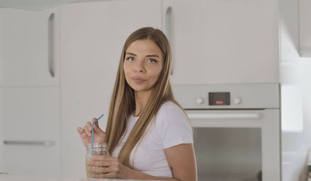 Young blond woman in white t-shirt drinks fruit smoothie and dan - Zdjęcie, obraz