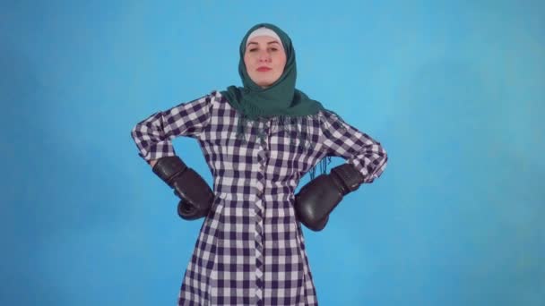 Young Muslim woman in Boxing gloves on a blue background looks at the camera - Metraje, vídeo