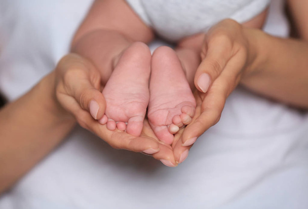 Mother holding feet of her cute little baby in hands, closeup - Fotó, kép