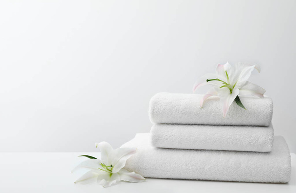 Pilha de toalhas frescas com flores na mesa contra fundo branco. Espaço para texto
 - Foto, Imagem
