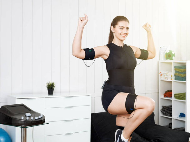 Una bella ragazza si sta allenando in un abito nero su un elettrico EMS
  - Foto, immagini