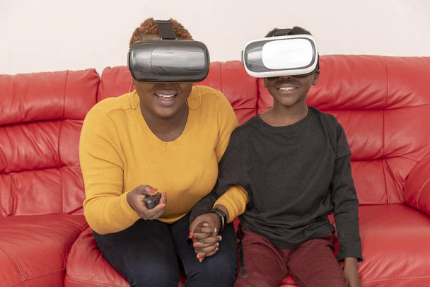Hampshire, Engeland, Verenigd Koninkrijk. April 2019, moeder en zoon dragen reality bril zittend op een rode leren bank - Foto, afbeelding