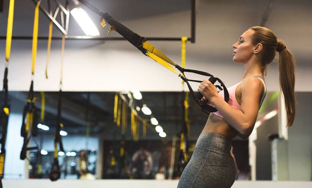 Young woman performing TRX training in gym, copy space - Photo, Image