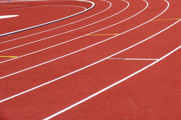 Красная беговая дорожка с белыми линиями на стадионе
 - Фото, изображение