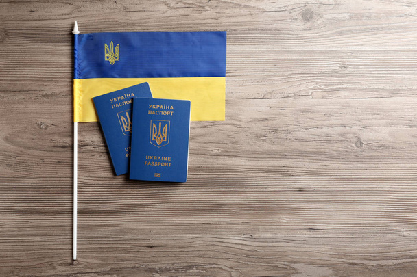 Ukrainian travel passports and national flag on wooden background, flat lay with space for text. International relationships - Foto, imagen