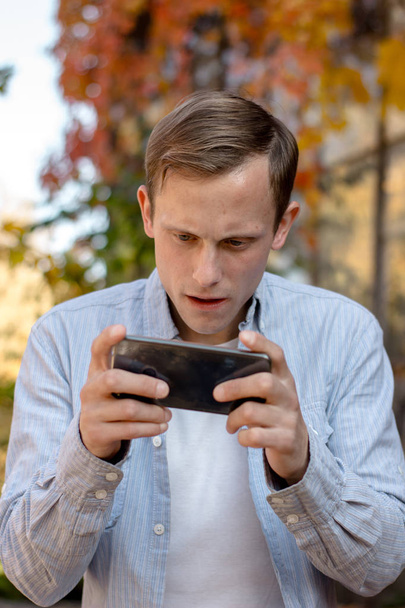 Portret faceta gra na telefon w luźnej odzieży w jesiennym parku - Zdjęcie, obraz