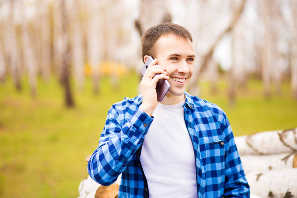 Şehir parkında yürüyen ve telefonuyla konuşan mutlu genç adamın görüntüsü. - Fotoğraf, Görsel