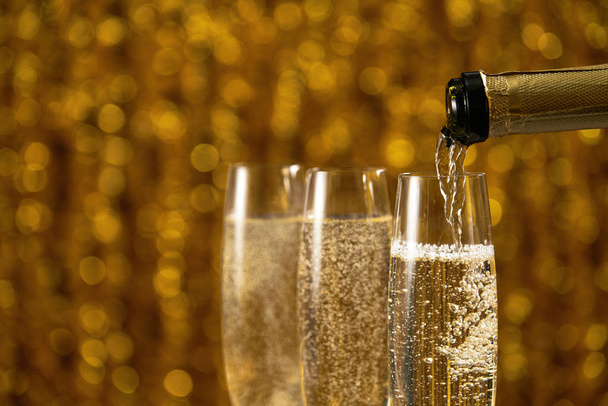 Pouring champagne into glass on golden stylish background with golden bokeh circles place for text - Photo, Image
