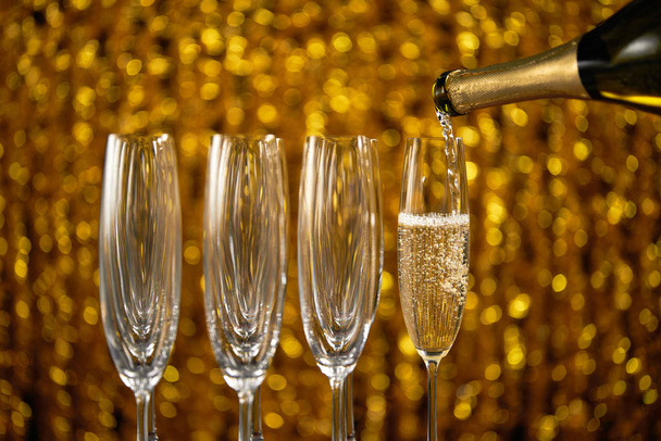Pouring champagne into glass on golden stylish background - Photo, Image