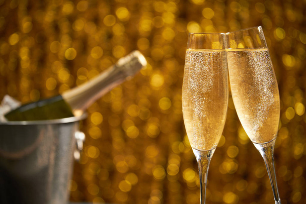 Полная бутылка шампанского в ведре со льдом и два бокала шампанского на фоне золотого боке
 - Фото, изображение