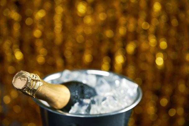 Бутылка шампанского в ведре со льдом на фоне золотого боке, избирательный фокус
 - Фото, изображение