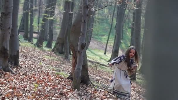kleine Barefoot meisje loopt in een bos of Park en verbergt achter bomen in een witte jurk met blauwe patronen. - Video