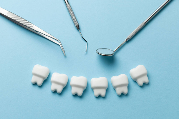Здоровые белые зубы на синем фоне и стоматологические инструменты зеркало, крюк
. - Фото, изображение