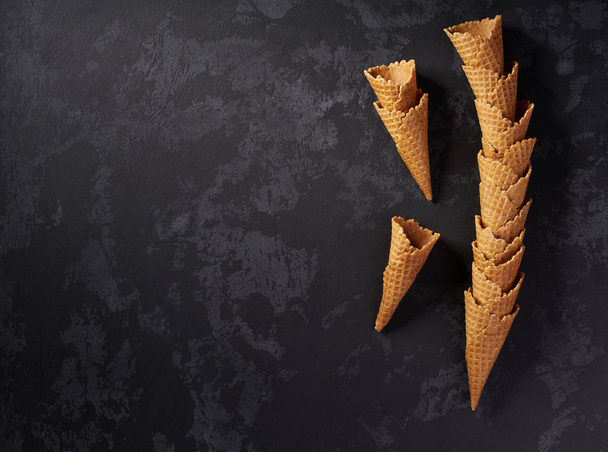 Bodegón de torre apilada de conos de helado de waffle vacíos sobre fondo oscuro, vista superior
. - Foto, Imagen
