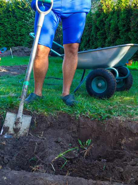 Mann gräbt Garten nach neuen Pflanzen und Schubkarre im Garten - Foto, Bild