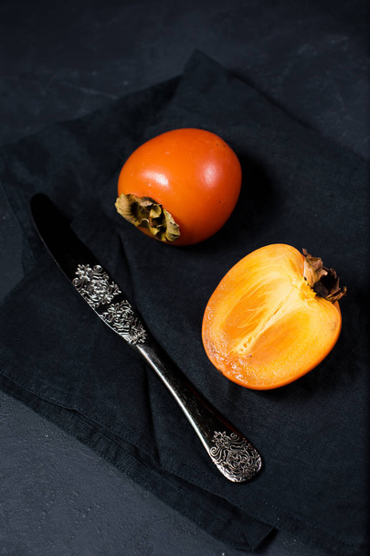 Ripe persimmon, knife on black background with space for text. - Photo, Image