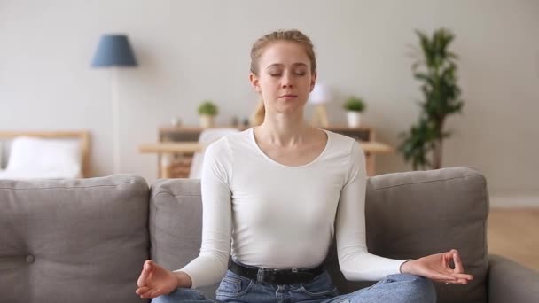 Calm serene woman sitting on couch meditating at home - Materiał filmowy, wideo