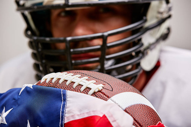 primer plano retrato de jugador de fútbol americano en casco con pelota y bandera americana orgulloso de su país, sobre un fondo blanco
. - Foto, Imagen