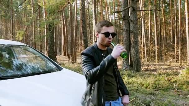 Opilý muž pije pivo u auta a vyhazuje v přírodě láhev. - Záběry, video