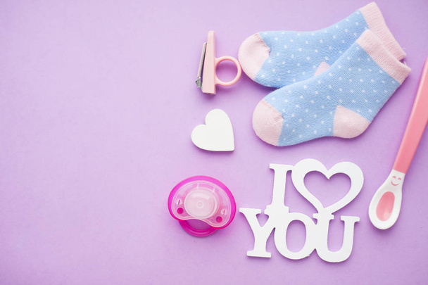 Newborn baby story. Strow heart and children's toys, scissors, baby bottle, nipple, hairbrush on violet background - Фото, изображение