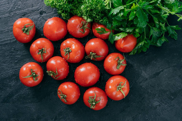 Lente vitaminen concept. Geoogst rode Heirloom tomaten en groene peterselie geïsoleerd over donkere achtergrond. Verse groenten voor het maken van salade - Foto, afbeelding