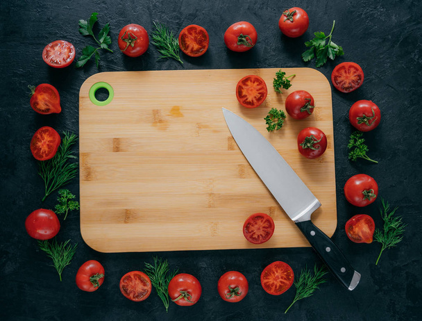 Ahşap doğrama tahtası etrafında yatan kırmızı domates yatay üst görünümü. Yeşil maydanoz ve dereotu. Bıçak yakın. Vegan masa. Gıda konsepti - Fotoğraf, Görsel