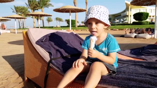 4k panning video di piccolo bambino ragazzo mangiare gelato su lettino a mare spiaggia
 - Filmati, video