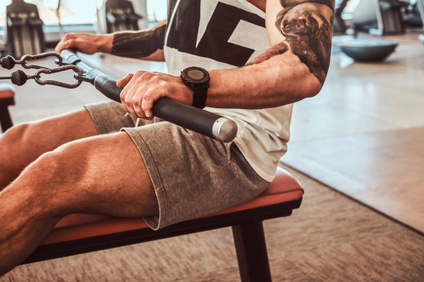 Jovem homem muscular com tatuagens está fazendo exercícios na máquina de remo
 - Foto, Imagem