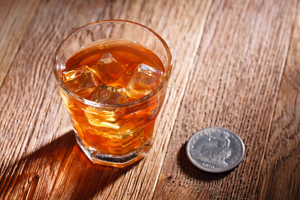 Glass of whisky and ice with old silver dollar on wooden table - Foto, imagen