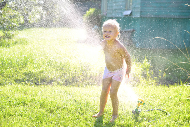 Child playing with garden sprinkler under trees - Foto, Bild