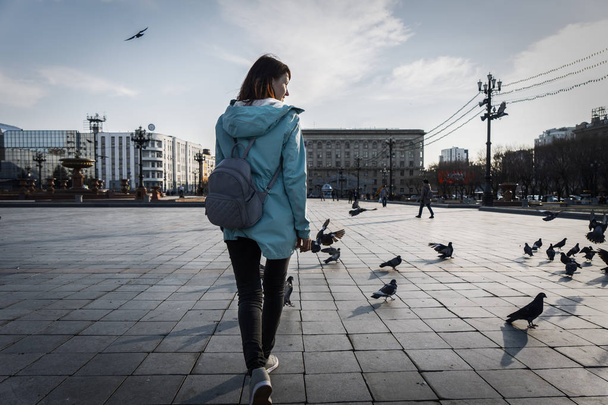 Street Photography: A girl tourist walks around the town square among pigeons. A backpack at the back. - Фото, зображення