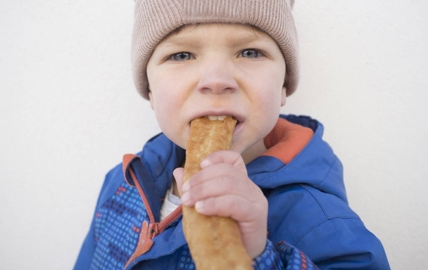 Little toddler biting traditional spanish churro outdoors - Photo, Image