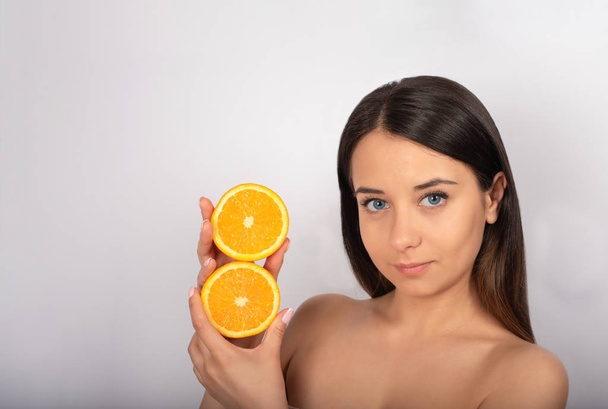 beautiful brunette girl, blue eyes, in her hand an orange, white background, close-up - Photo, Image