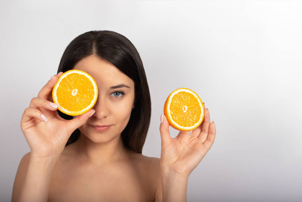 beautiful brunette girl, blue eyes, in her hand an orange, white background, close-up - Фото, изображение