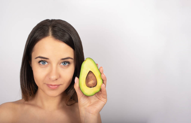 beautiful brunette girl, blue eyes, in hand avocado, white background - Photo, Image