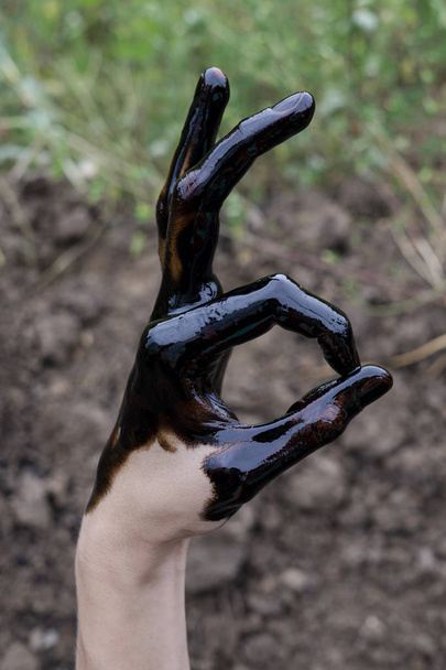 oil leaking. Very dirty hand.Stain hands showing thumbs up with black oil on soil background. hand showing OK - Φωτογραφία, εικόνα