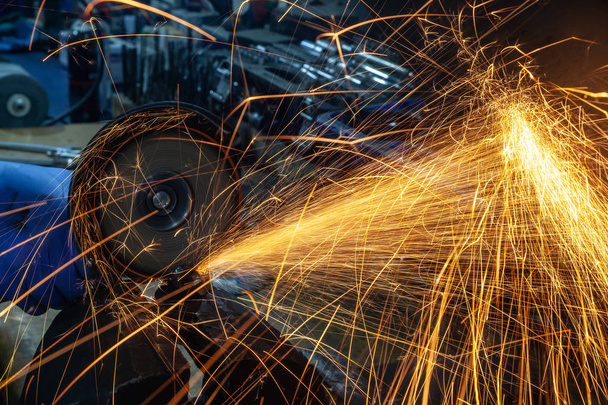 Close-up of a man sawing   bearing metal with a hand circular saw, bright flashes flying in different directions, in the background tools for an auto repair shop. Work of auto mechanics. - Photo, Image