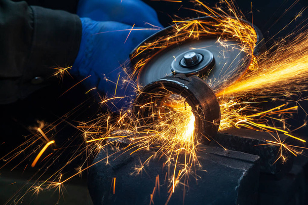 Close-up van een man zagen dragende metalen met een hand cirkelzaag, heldere flitsen vliegen in verschillende richtingen, in de achtergrond-hulpmiddelen voor een auto reparatiewerkplaats. Werk van auto mechanica. - Foto, afbeelding