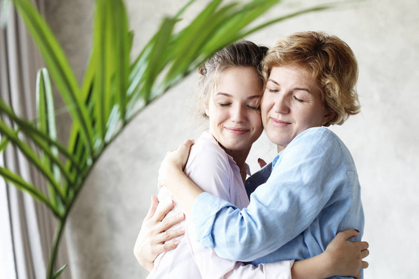 lifestyle and people concept - Beautiful senior mom and her adult daughter are hugging, looking at camera and smiling. - Foto, afbeelding