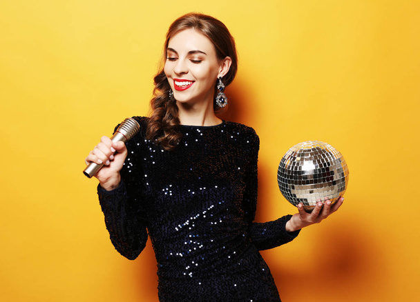 lifestyle and people concept - woman in evening dress holding microphone and disco ball - Photo, Image