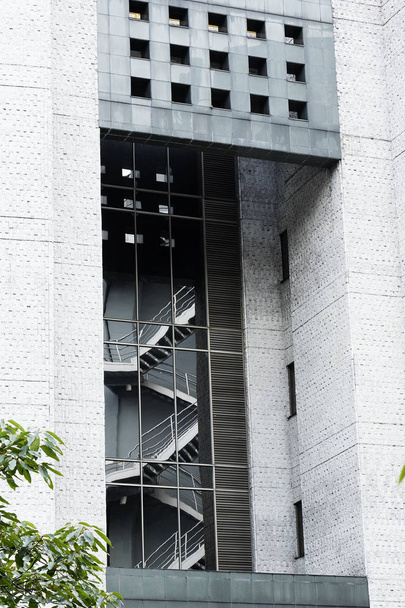 Reflejo de escaleras de emergencia en los vidrio de un edificio Moderno con Paredes de Cemento Gris Arquitectura Moderna y profundidades en el edificio con Plantas Verdes en La Esquina Final Izquierda - Foto, afbeelding