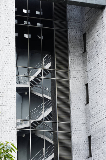 Reflejo de escaleras de emergencia en los vidrio de un edificio Moderno con Paredes de Cemento Gris Arquitectura Moderna y profundidades en el edificio con Plantas Verdes en La Esquina Final Izquierda - Foto, afbeelding