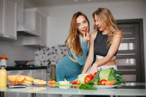 Two sports girl in a kitchen with vegetables - Фото, зображення