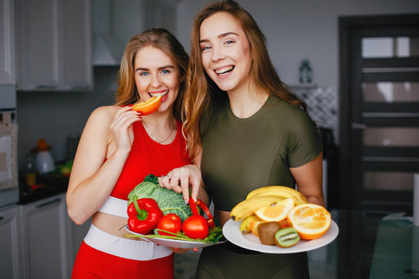 Two sports girl in a kitchen with vegetables - Фото, зображення