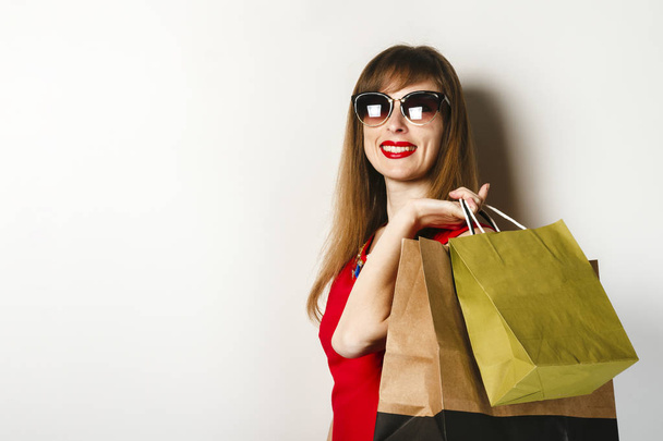 Mladá dívka v červených šatech má v rukou balíčky po nakupování na světlém pozadí. Koncepce prodeje, nákupy. - Fotografie, Obrázek