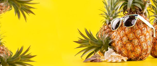 Creative pineapple looking up with sunglasses and shell isolated on yellow background, summer vacation beach idea design pattern, copy space close up - Фото, изображение