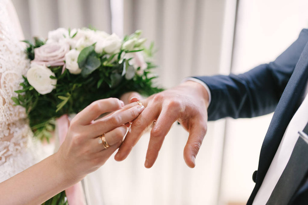 The bridegroom puts the wedding ring on the bride close up. The bride puts the bridegroom on the wedding ring. - Photo, image