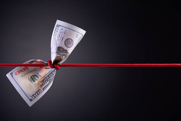American dollar tied up in red rope knot on dark background with copy space. business finances, savings and bankruptcy concept. - Photo, Image