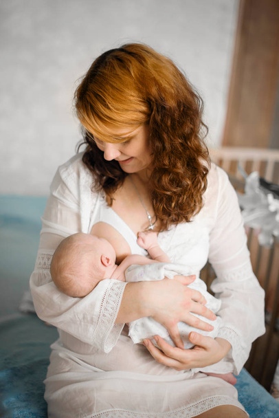 A amamentar. Bela mãe ruiva amamenta um bebê recém-nascido. Fotos de aparência natural
 - Foto, Imagem